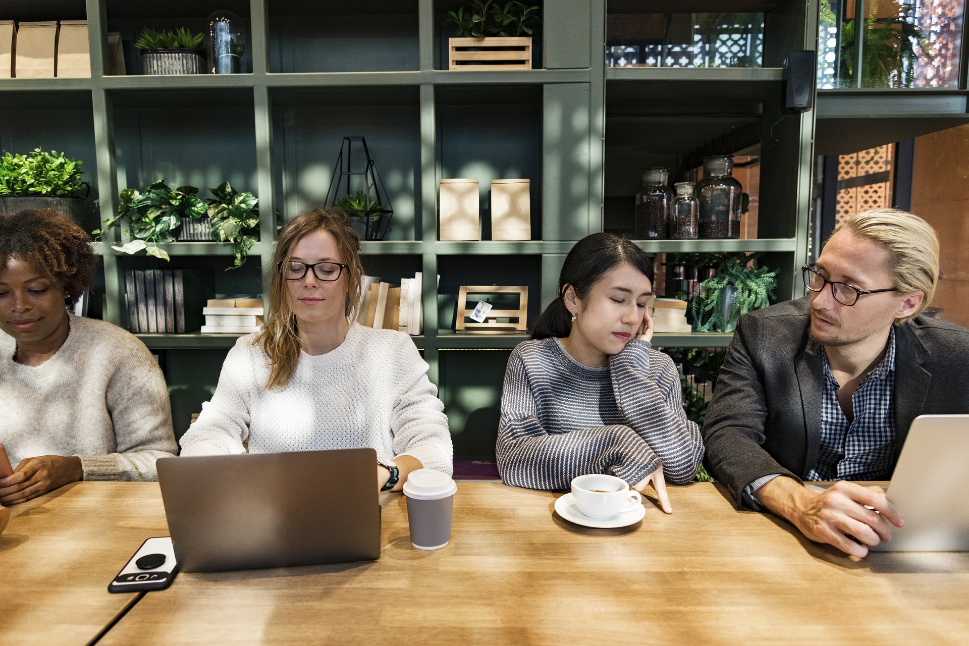 four people sitting at large desk with computers