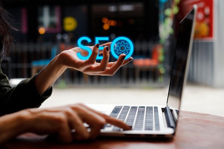 A person working on their laptop. They're holding their hand out, and the letters "SEO" were digitally added to the photo.